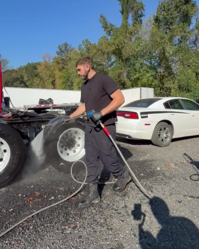 Mustafa pressure washing the rear wheels of a semi tractor in a gravel truck yard