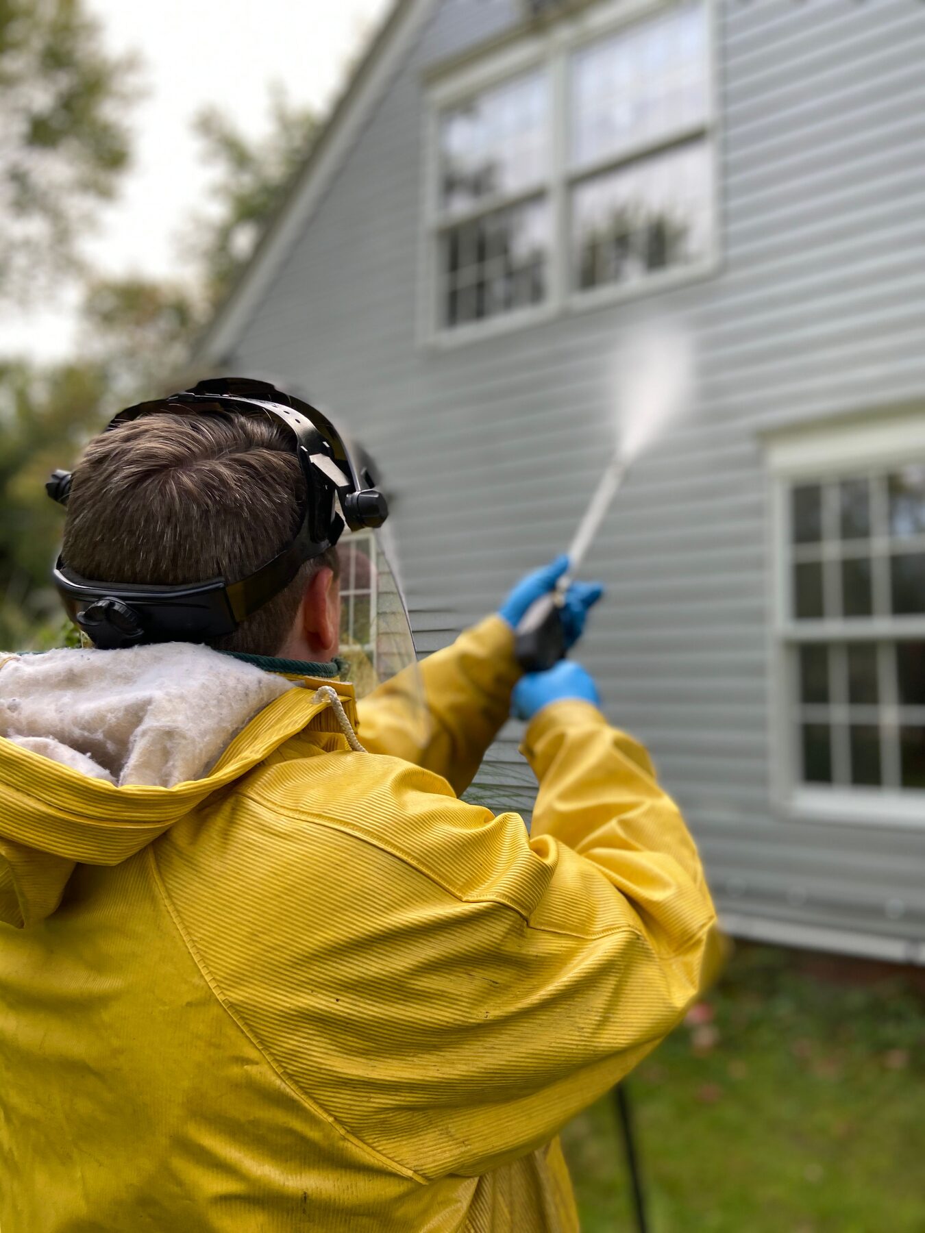 Washing the grey siding of a two-storey house with a spray wand