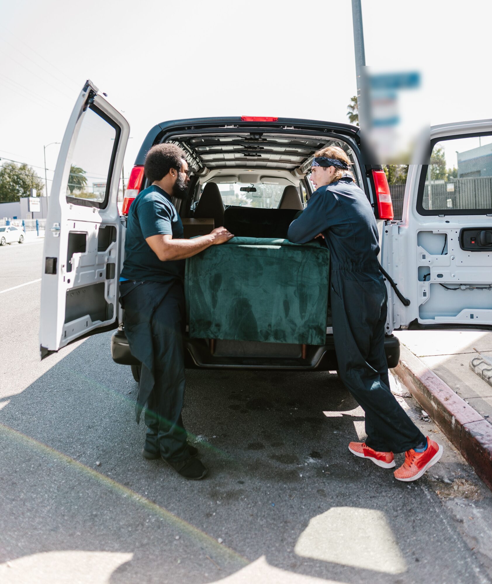 Two workers in dark uniforms loading a green couch into the back of a white van